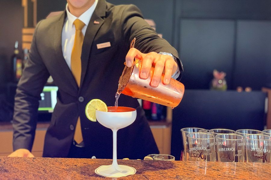 Barkeeper im Anzug gießt einen Cocktail aus dem Kupfershaker in eine weiße Schale mit Limettenscheibe