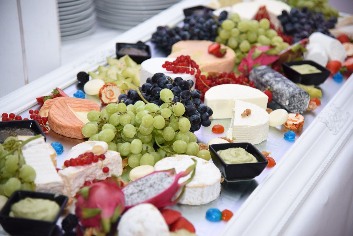Buffet mit Käsesorten, Trauben, Drachenfrucht und Dips auf einem weiß gerahmten Spiegeltablett