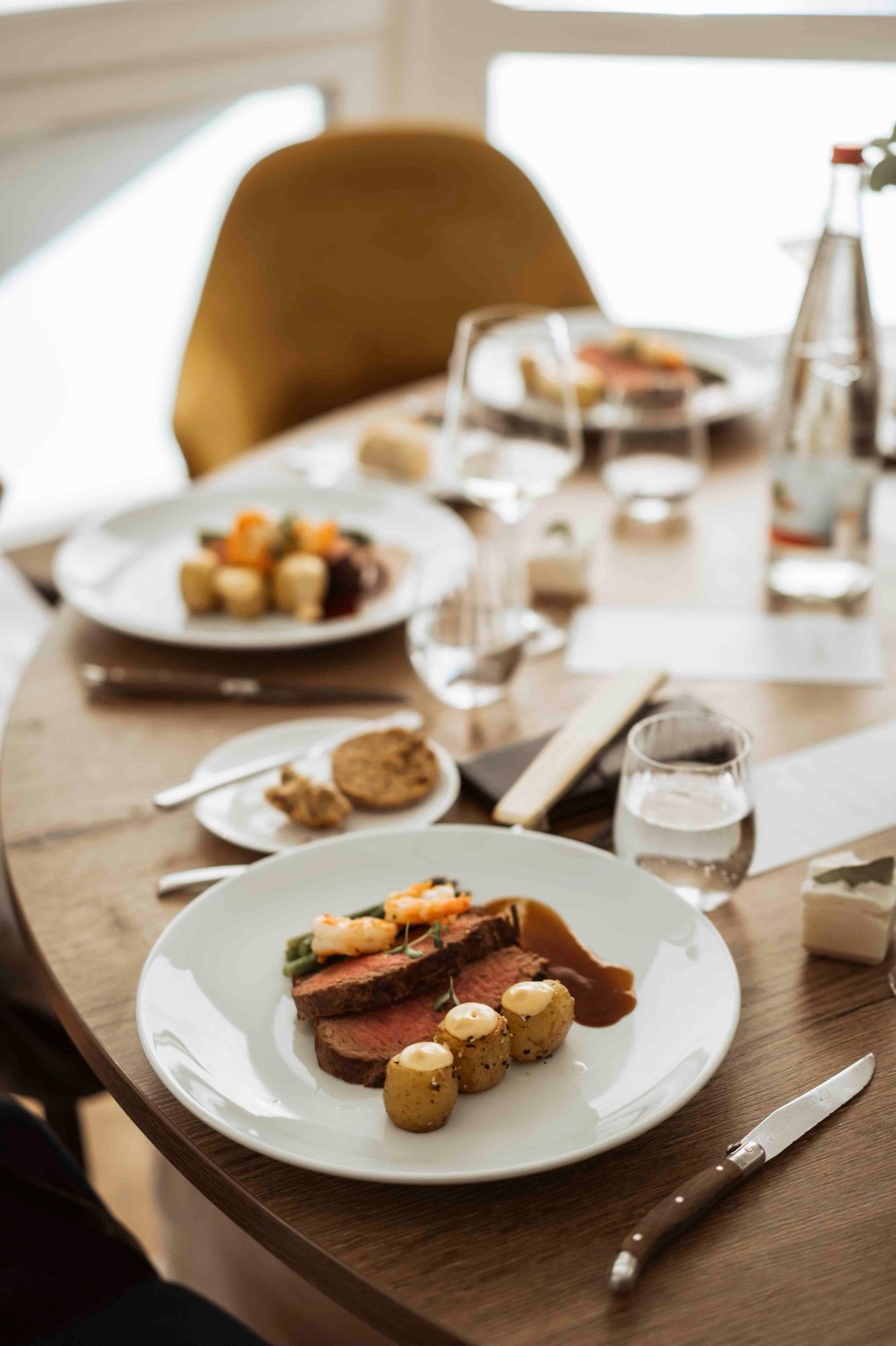 Hochzeitsmenü: Teller mit rosa gebratenem Fleisch, Garnele, Gemüse und kleinen Kartoffeln auf einem gedeckten Tisch
