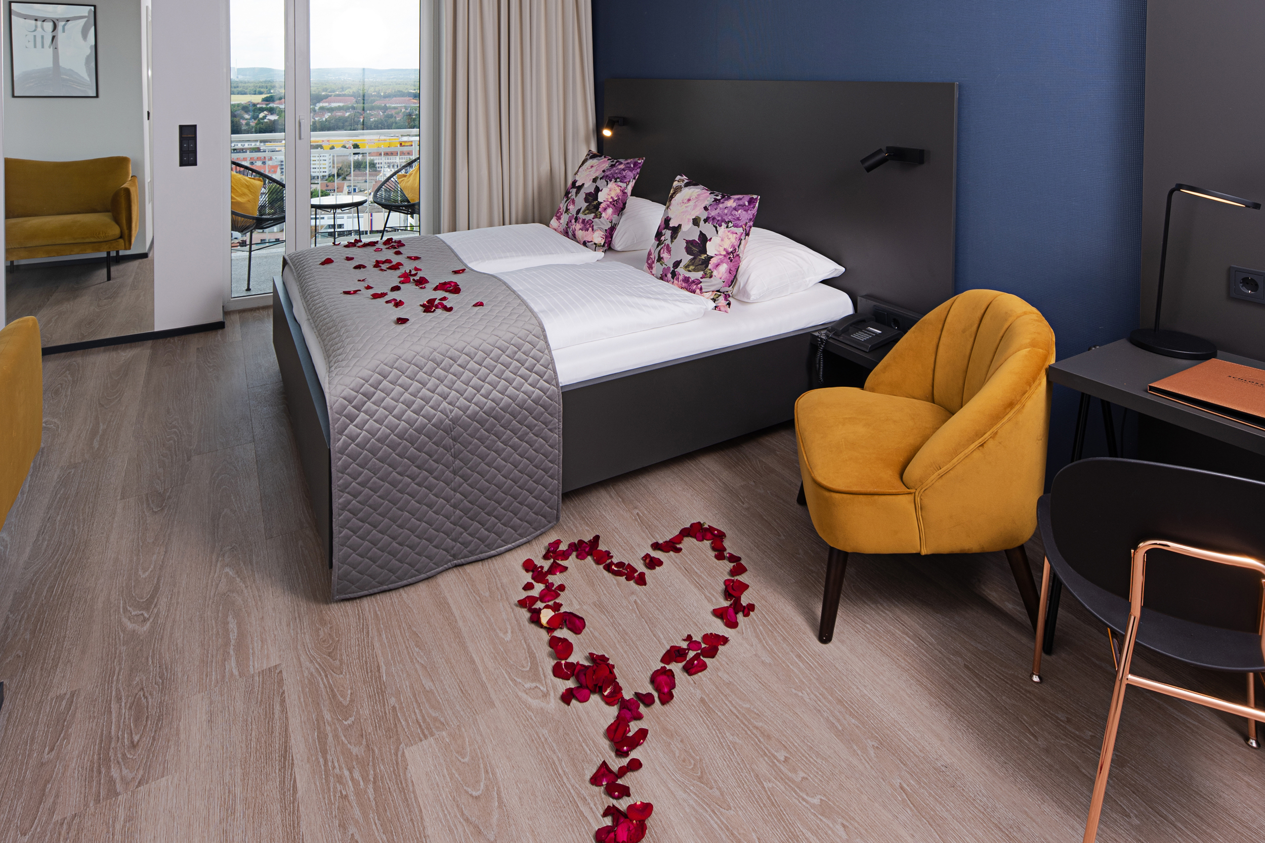Romantisch dekoriertes Hotelzimmer mit Rosenblättern in Herzform auf dem Boden und auf dem Bett, modernes Interieur