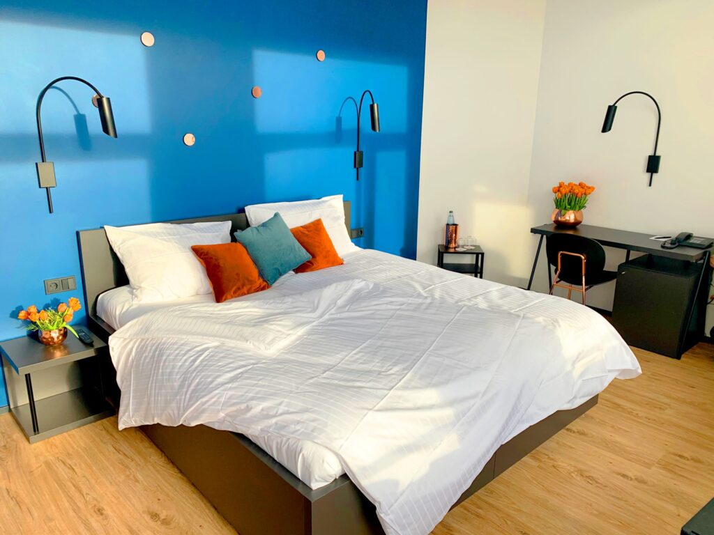 Bett vor einer blauen Wand im Deluxe Zimmer mit farbigen details und Tulpen als Dekoration