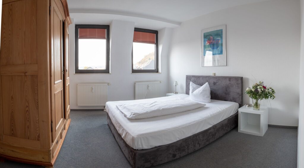 Apartment des Schlossberg Hotels mit ca 51qm mit geräumigem Schlafbereich und Kingsize Bett mit rustikalem Kleiderschrank aus Holz