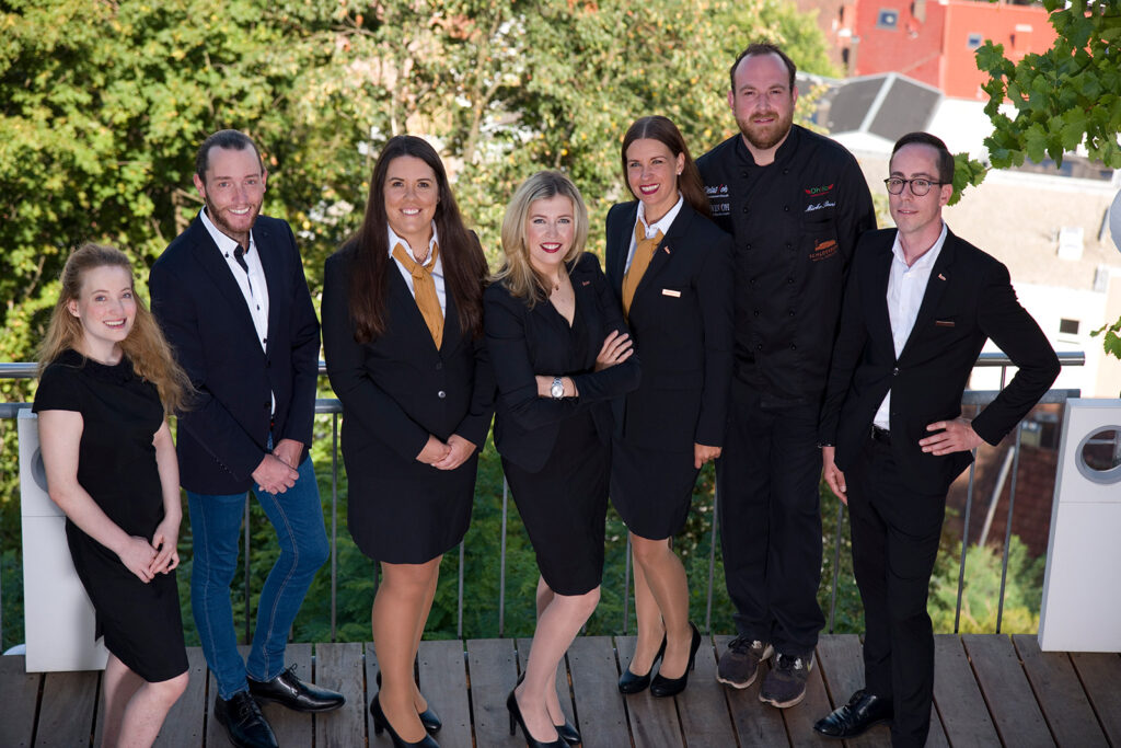 Aufname von Mitarbeiter/innen des Schlossberg Hotels in Arbeitskleidung lächelnd in die Kamera schauend