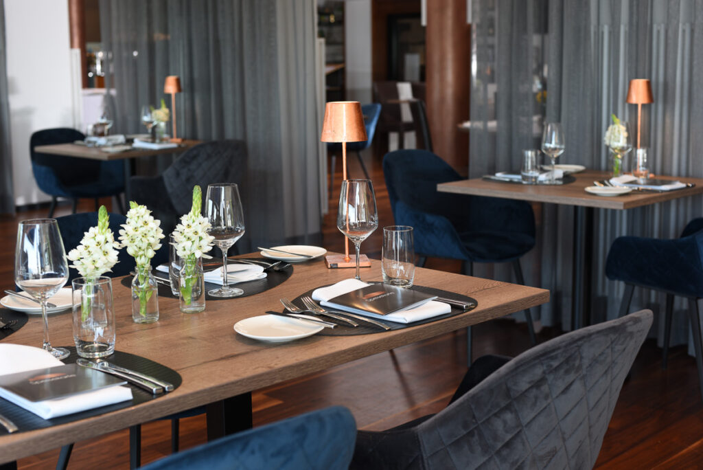 Gedeckter Tisch im Anschnitt auf der linken Seite im Restaurant mit Blumen in Vasen und kupferfarbenen Lampen auf den Tischen
